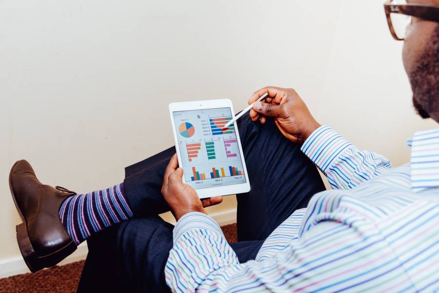 Man sits at desk, holds Ipad in hand and evaluates statistics