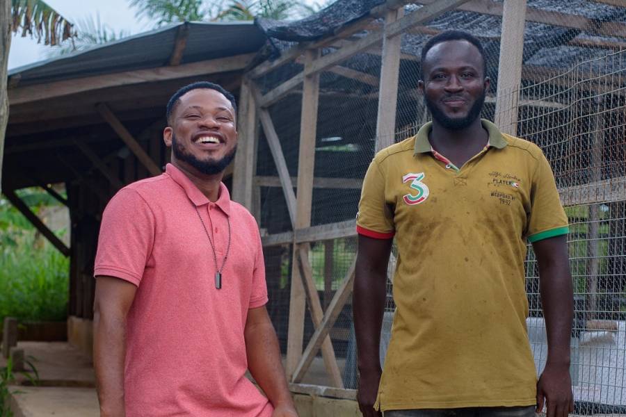 Kwasi and his employee stand in front of his Infinity Farm building