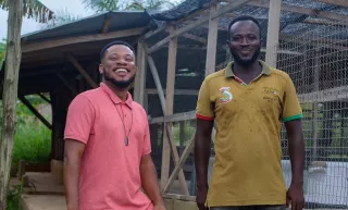 Kwasi and his employee stand in front of his Infinity Farm building
