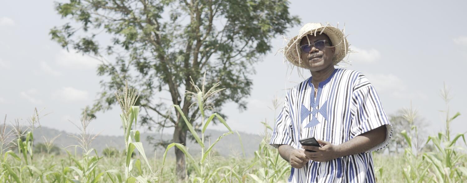 Togolese Entrepreneur who was supported through WIDU.africa Project stands in his field while holding a smartphone