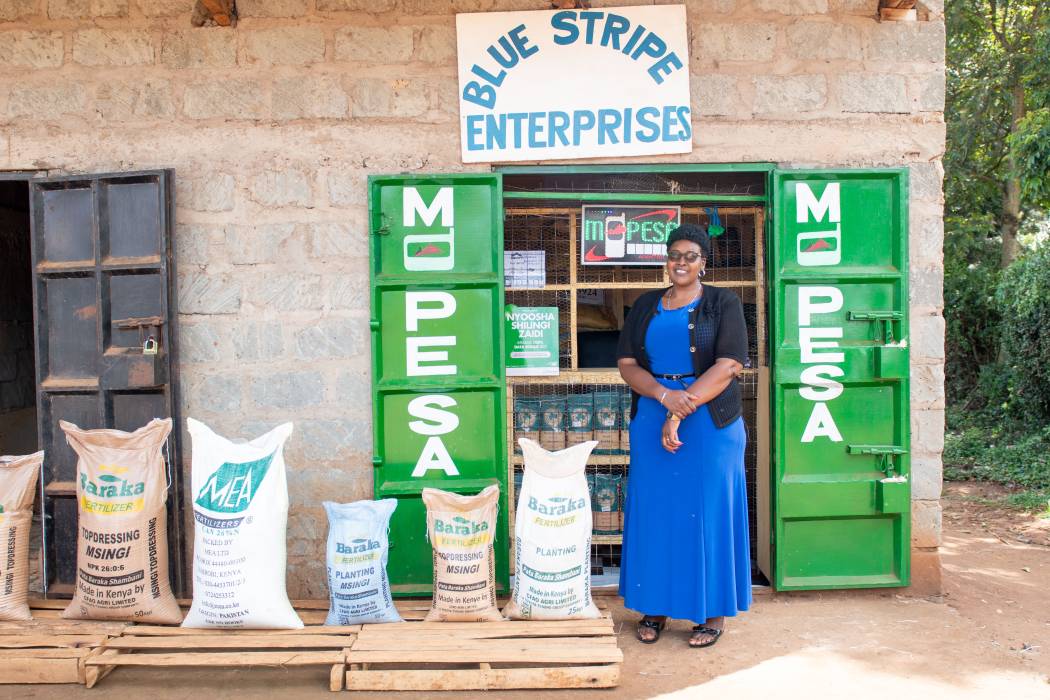Beatrice Nduta, owner of Kenyan business Blue Stripe Enterprises stands in front of her shop and presents stock she sells.