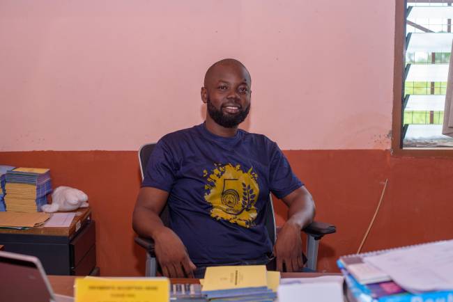 Headmaster of Discovery Bay International School Kingsley Dzidzor Afetorgbor sits in his office and smiles into the camera